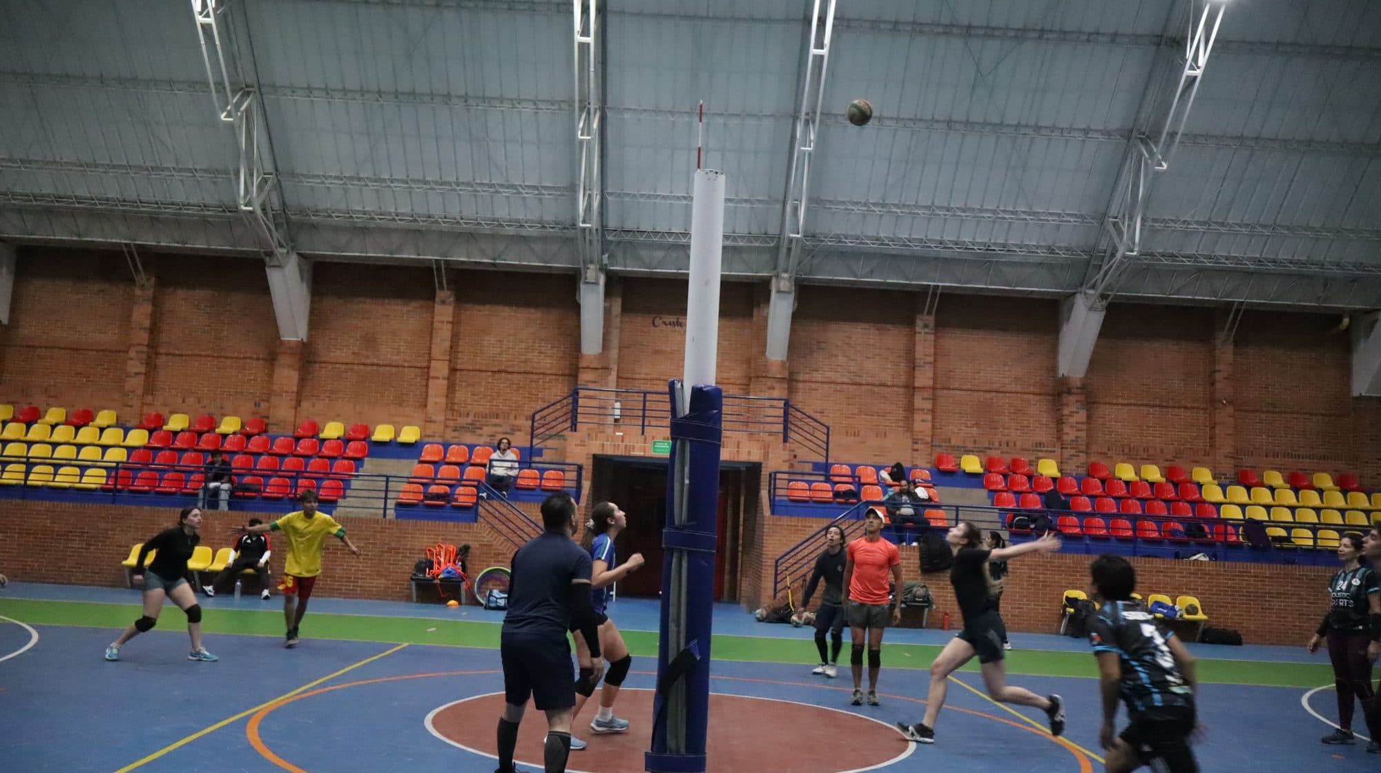 Partido de voleibol en un coliseo cubierto con graderías de colores